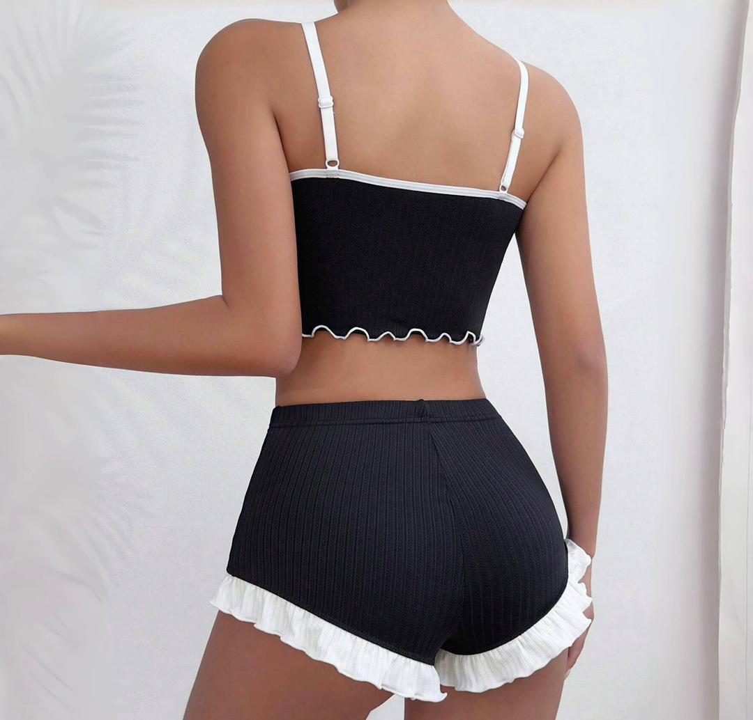 Black ribbed pajama set with white ruffle trim on shorts and adjustable straps, sleek and modern sleepwear style.
